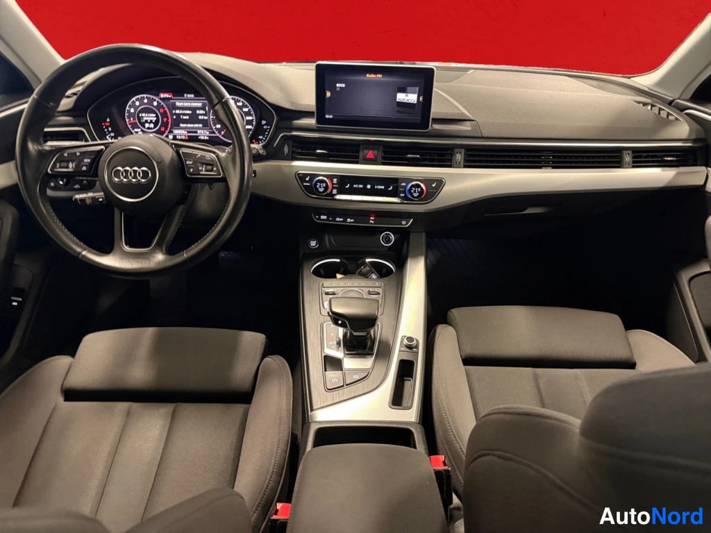 Yksityiskohta: Audi A4:n ohjaamo suoraan edestä: Audi-merkkinen ohjauspyörä, diginäyttö, infotainment-näyttö, automaattivaihteen valitsin ja kaksivyöhykeilmastointi.