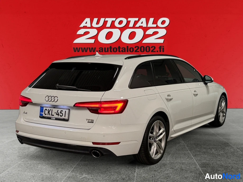 Takaviisto: Valkoinen Audi A4 -farmari takaviistosta vasemmalle katsottuna punaisella taustalla.