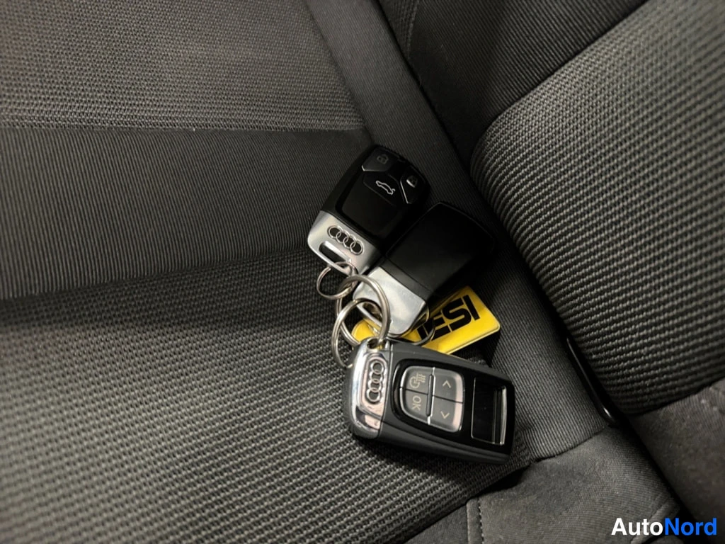 Muu: Kaksi Audi-avainpaaria ja keltainen avainnappi tummalla kankaalla penkillä.