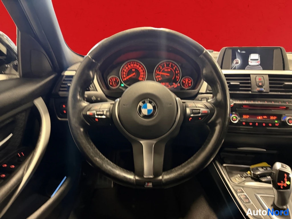 Edestä: Interiör: BMW-ratt, instrumentpanel ochcenterkonsol framifrån; röd bakgrund.