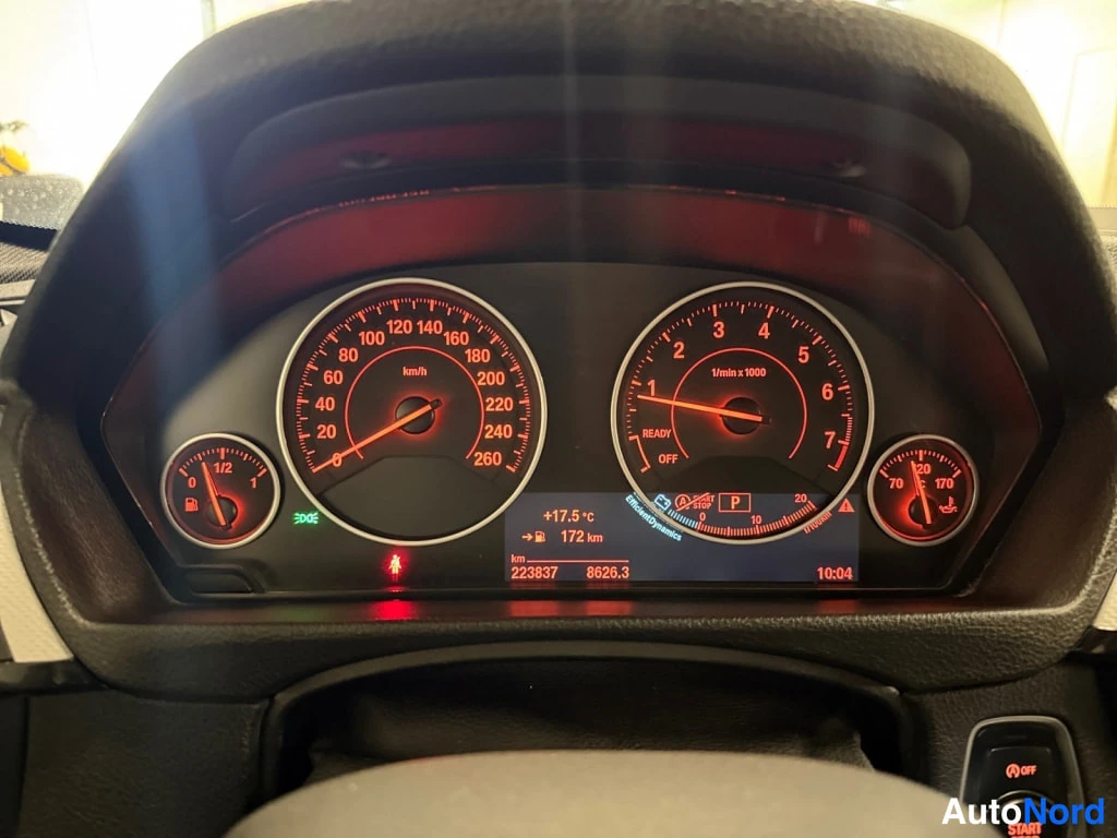 Edestä: Interiör: BMW-ratt, reda instrument, display och centerkonsol; röd bakgrund.