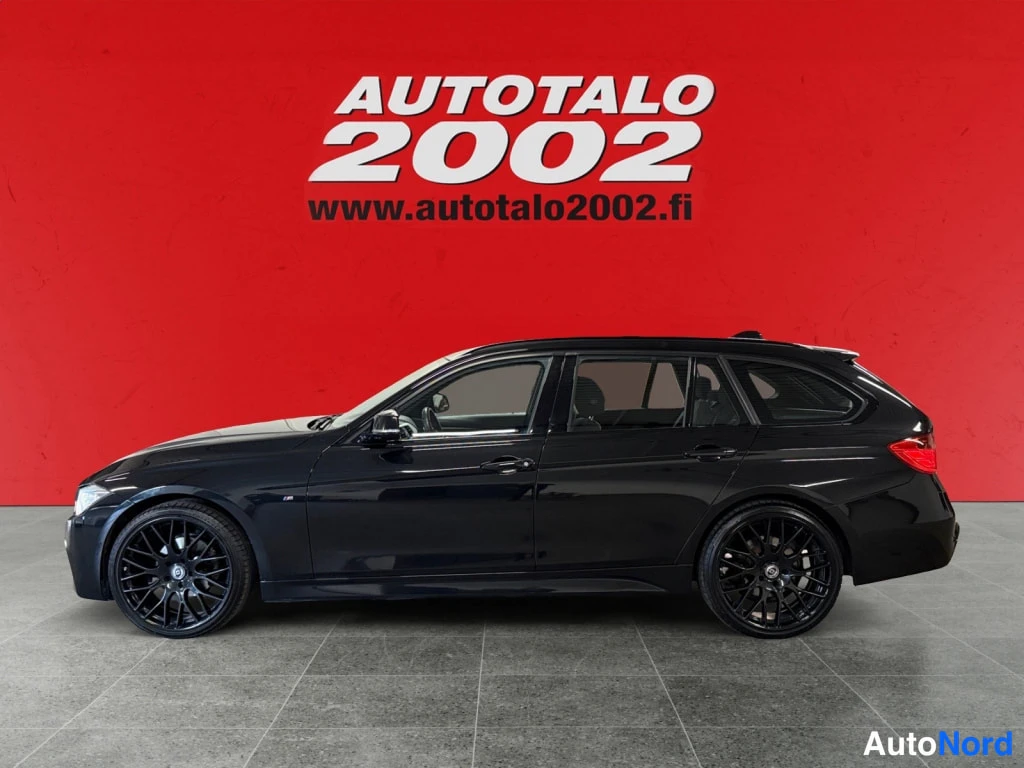 Sivulta: Mustan farmariauto BMW:n sivuprofiili punaisella taustalla; rekisteritunnus ei näy. Kuva: Autotalo 2002 -logotiili.
