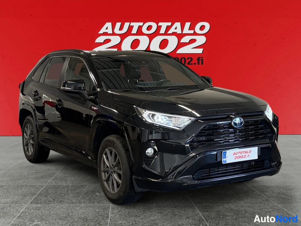Etuviisto, nokka oikealle: Mustan Toyota RAV4:n etukulma, keulaa ja oikeaa kylkeä, punaisella Autotalo 2002 -taustalla.