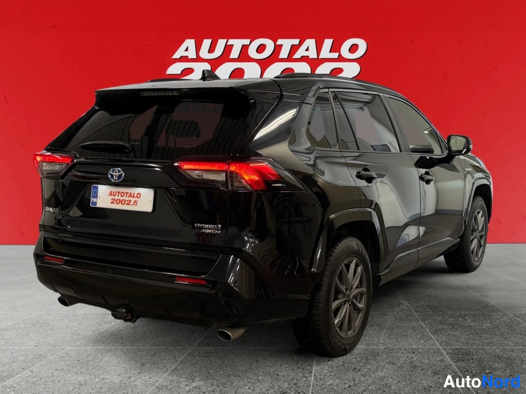 Takaviisto: Mustan Toyota RAV4:n takakulma, takavalot, tavaratilan luukku ja pyyhinloukku punaisella taustalla.