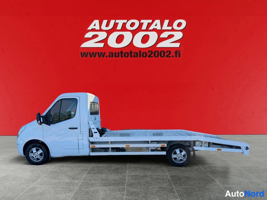 Etuviisto, nokka vasemmalle: Renault Master -alustavalokuvaajavaunu sivulta, valkoinen, lava-alustalla, punainen tausta