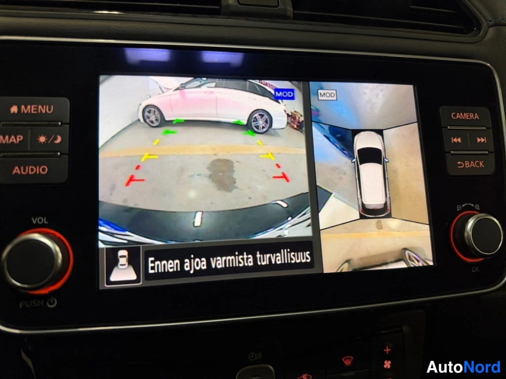 Muu: Autoon kiinnitetty infotainment-näyttö, jolla näkyy kahtaaloittainen ympäriview-kamerakuva: vasemmalla etukameran kuva ja ohjausviivat, oikealla ylhäältäpäin ku