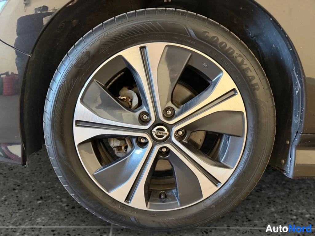 Yksityiskohta: Lähikuva auton pyörästä: tumma kevytmetallivanne Nissan-merkillä ja Goodyear-renkus