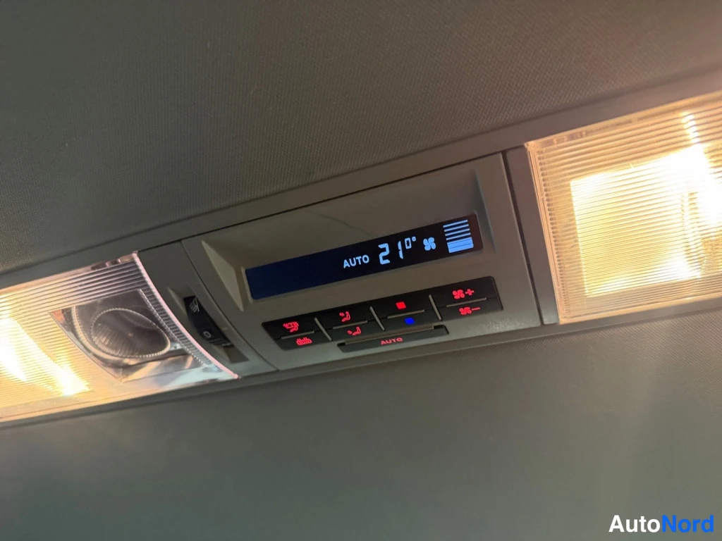 Yksityiskohta: Kattohallin sisäinen ilmastointipaneeli, jonka näyttö näyttää 'AUTO 21°', ja sen alla joukko punaisia painikkeita.