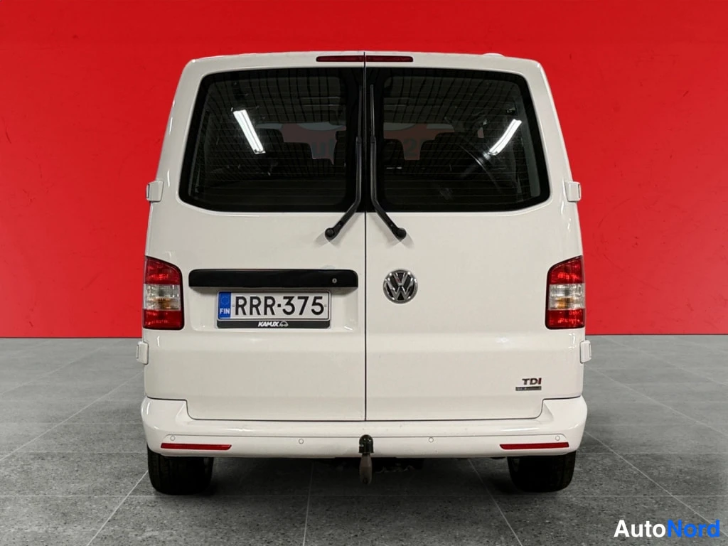 Takaa: Valkoisen Volkswagenin taka-näkymä, rekisterikilpi, VW-merkki ja takaovet punaisen taustan edessä.