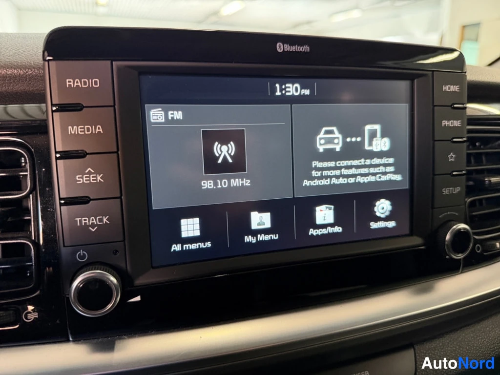 Muu: Kia-auton radio-/multimedianäyttö näyttää FM-radioita taajuudella 98.10 MHz; näytön teksti mainitsee Android Auton ja Apple CarPlayn tuen, Bluetooth-merkki näyt