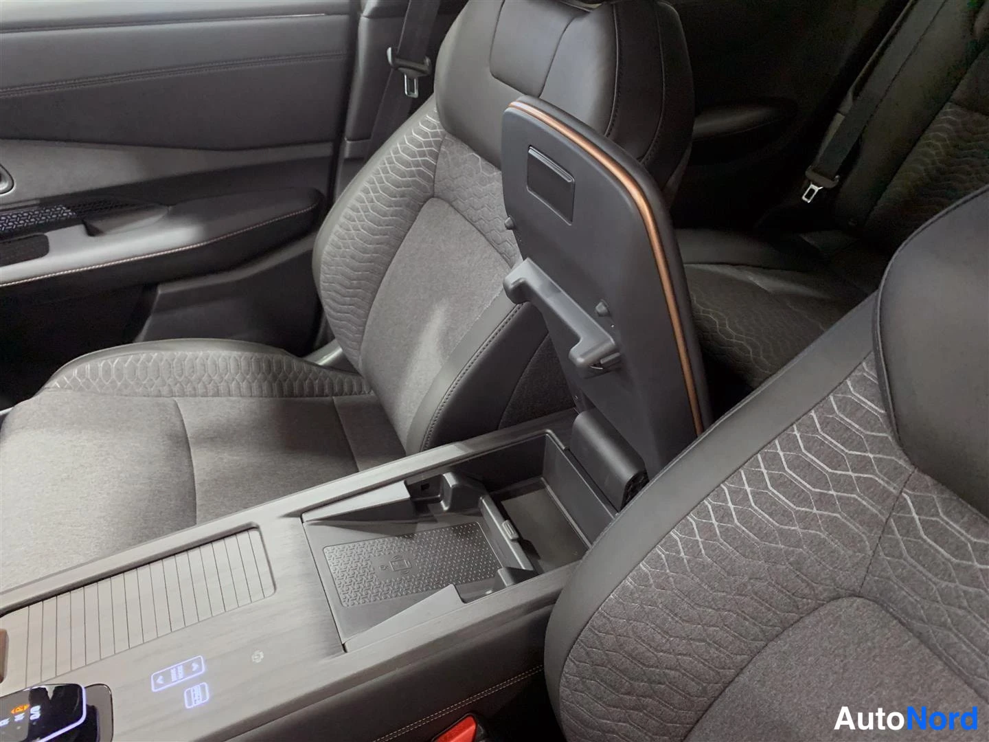 Etuviisto: Nissan Ariyan sisätilat: etupenkin selkänoja ja istuinpetsaus näkyvät keskikonsolin, armrest-lokeron ja kuljettajan ovenkarmeiden kanssa. Keskikonsolissa lampun