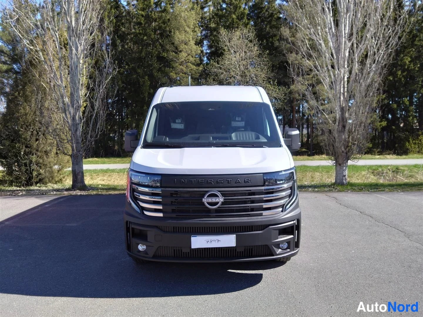 Edestä: Valkoinen Nissan Interstar -pakettiauto suoraan edestä kuvattuna, kyltit INTERSTAR ja NISSAN-koriste säleikössä.
