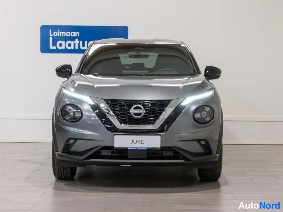 Edestä: Nissan Jukein etupää edestä kuvattuna harmaana, erikoiset pyöreät sumuvalot ja Nissan-merkki etusäleikössä.
