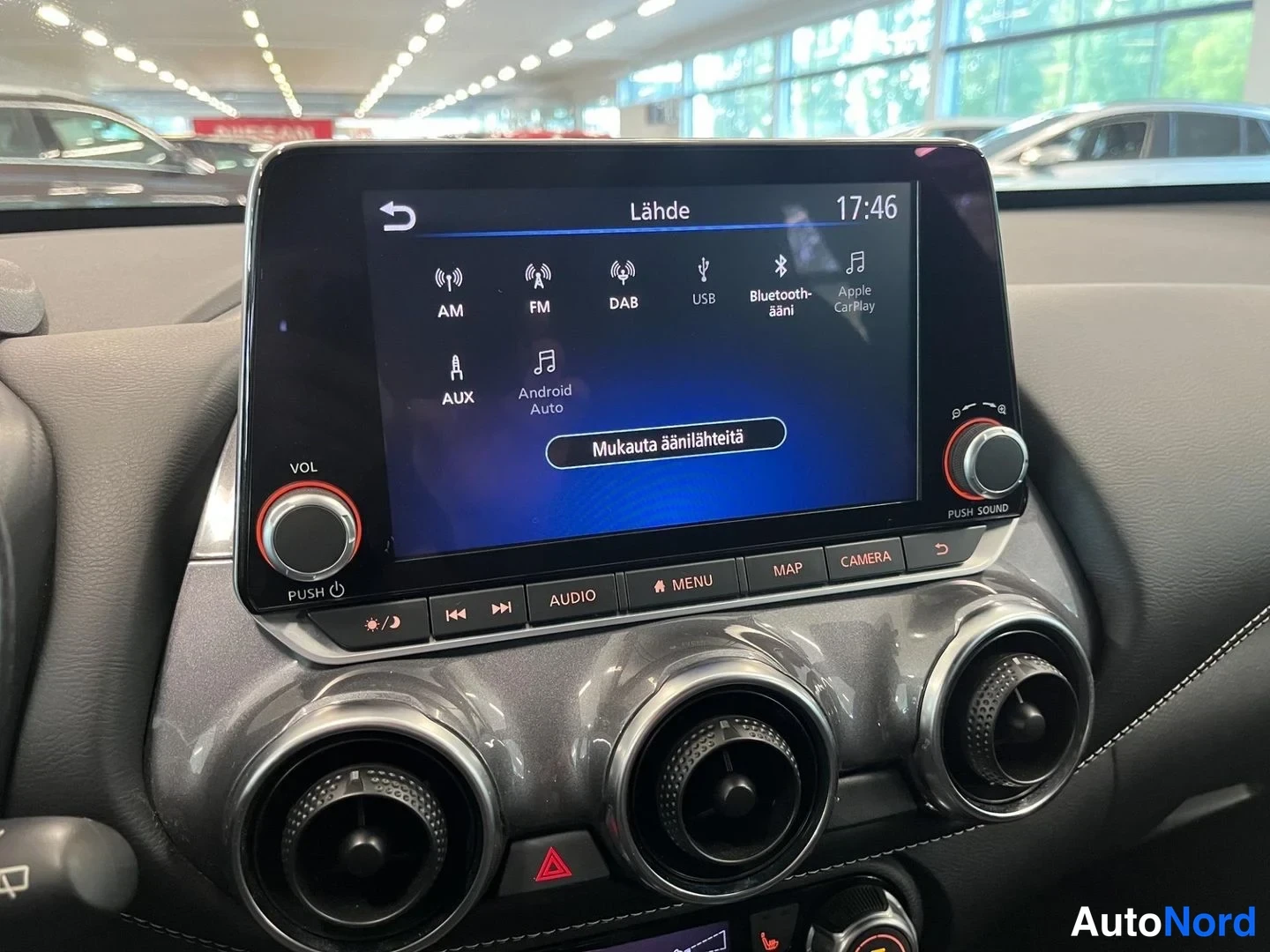 Muu: Auton kojelaudan infotainment-näyttö lähikuva; lähdetaulukko AM, FM, DAB, USB, Bluetooth-ääni, Apple CarPlay, AUX ja Android Auto -kuvakkeineen, alla AUDIO-, ME