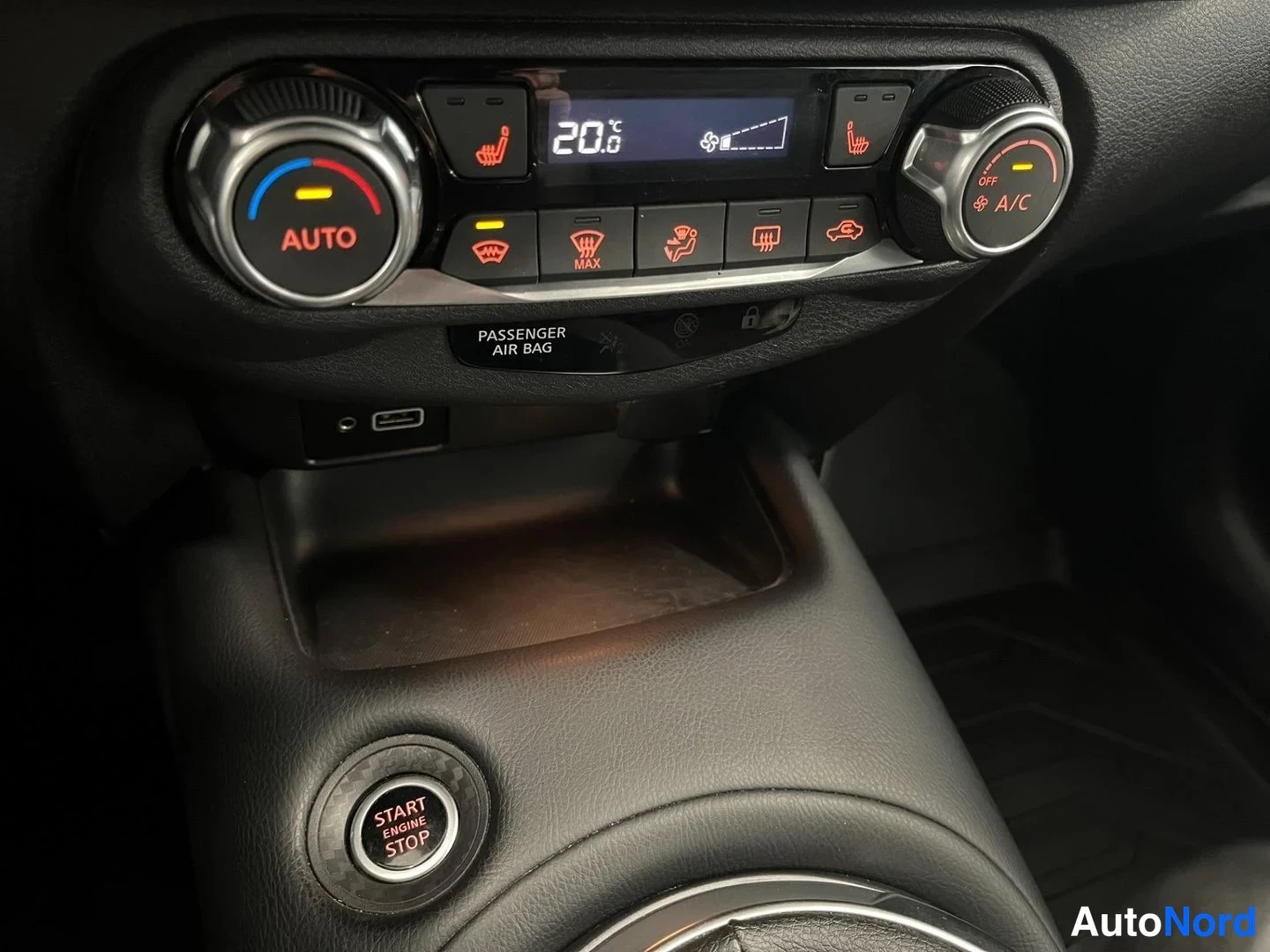 Yksityiskohta: Lämmityksen/kauko-ohjauksen paneeli: näytössä '20.0', AUTO-merkitty lämpötilapyörä, A/C-painike, istuinten ja tuulilasin lämmityspainikkeet, teksti 'PASSENGER A