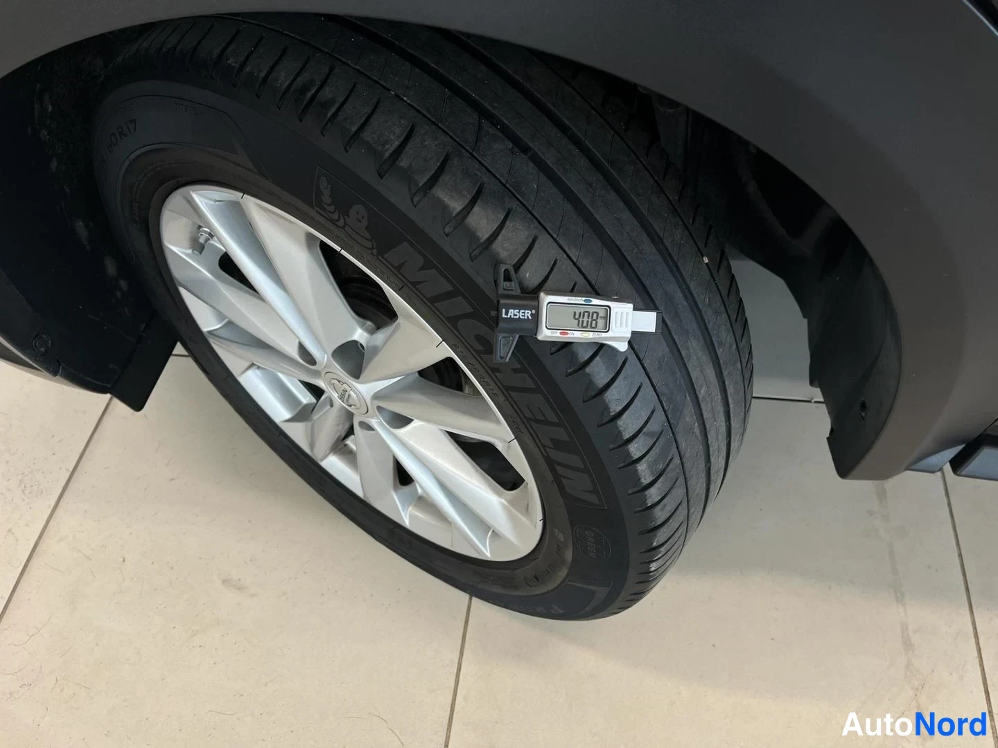 Yksityiskohta: Auton takapyörän lähikuva: hopeiseksi maalattu kevytmetallivanne ja Michelin-kesärenkaaseen kiinnitetty Laser-uramittari, näytössä lukema 4,08 mm