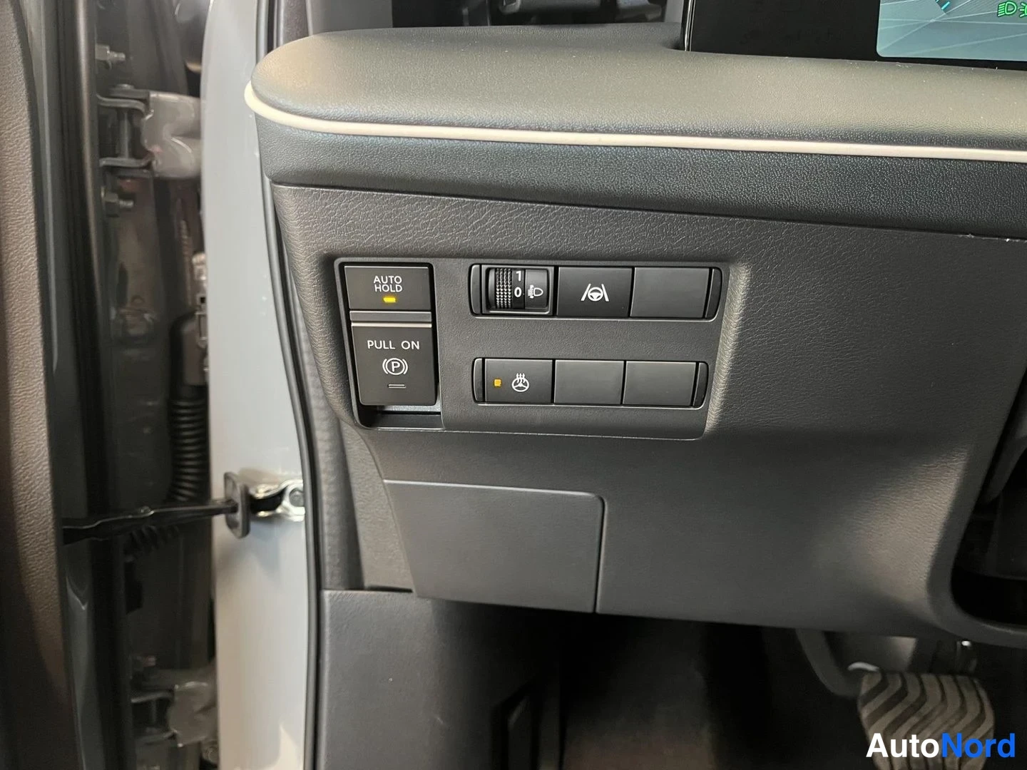 Yksityiskohta: Kojelaudan alaosan kytkimiä: sähköinen käsijarru (PULL ON, P), AUTO HOLD -painike ja valaistuksen säädin. Oven avaama näkymä.