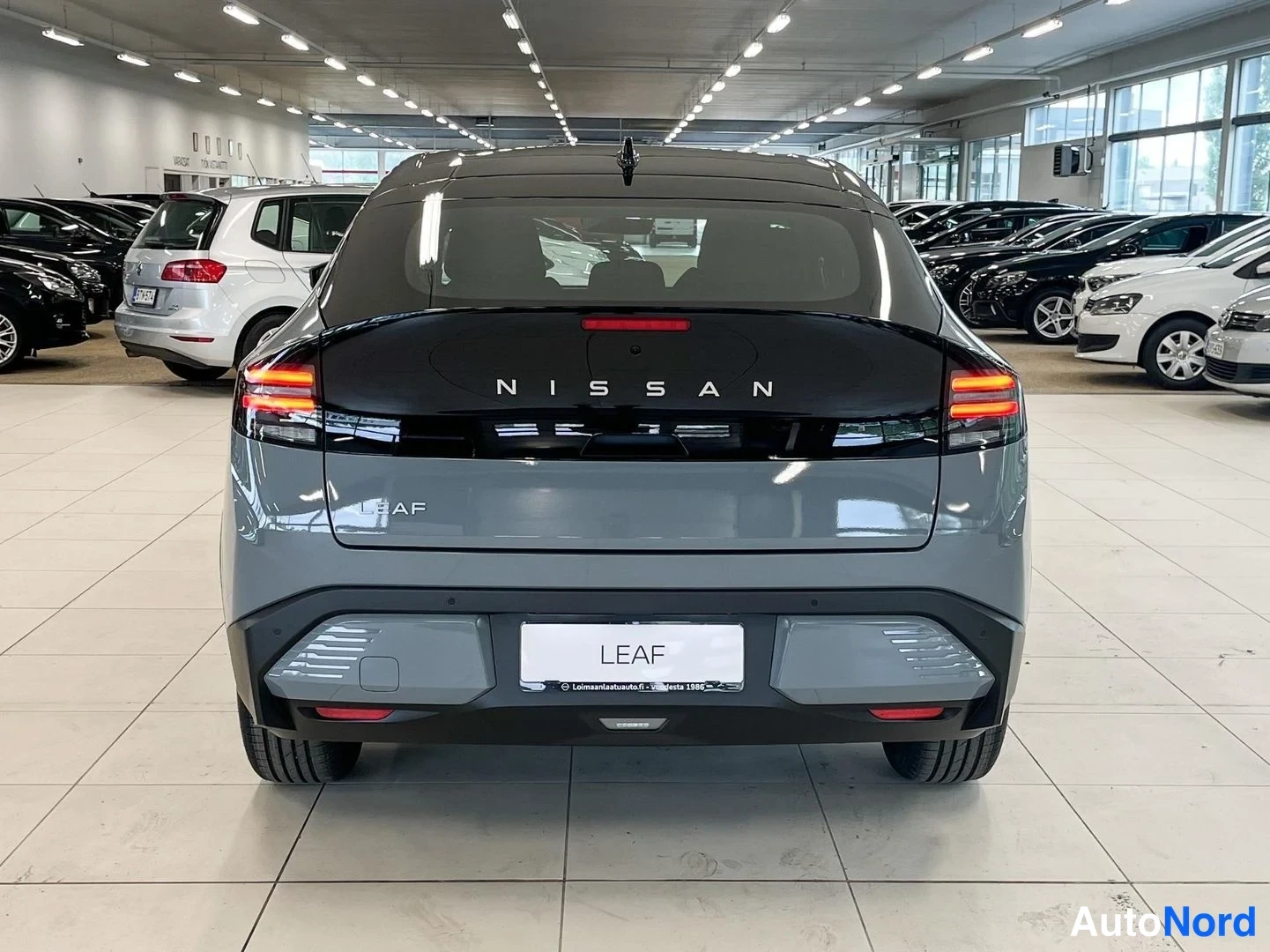 Takaa: Rear view of a grey Nissan Leaf. The rear boot lid displays the text NISSAN and LEAF, with a license plate reading LEAF.