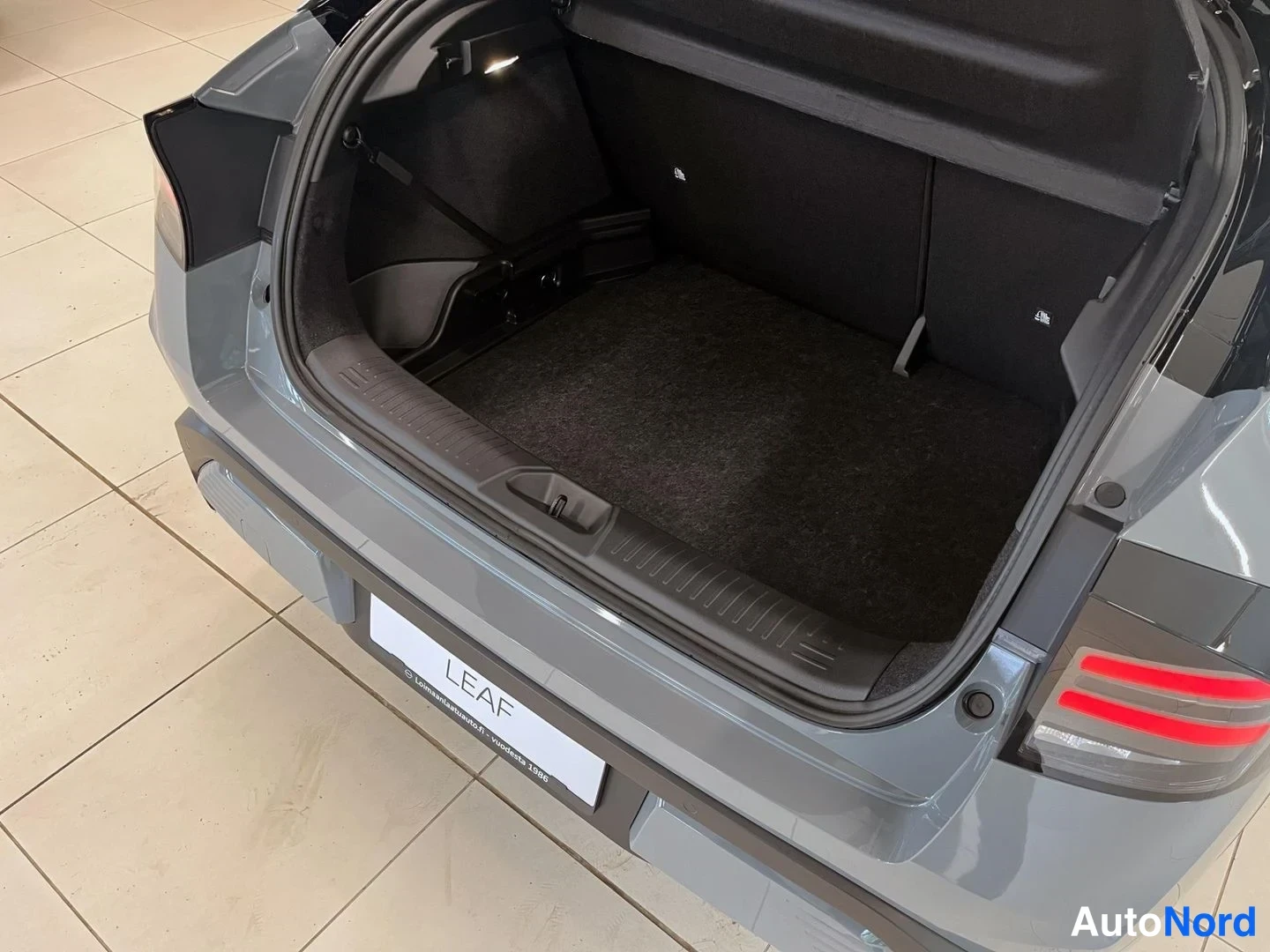 Takaa: Nissan Leafin takaluukku on auki ja kuvassa näkyy tyhjä tummaverhoiltu tavaratila, takapuskuri ja takavalo.