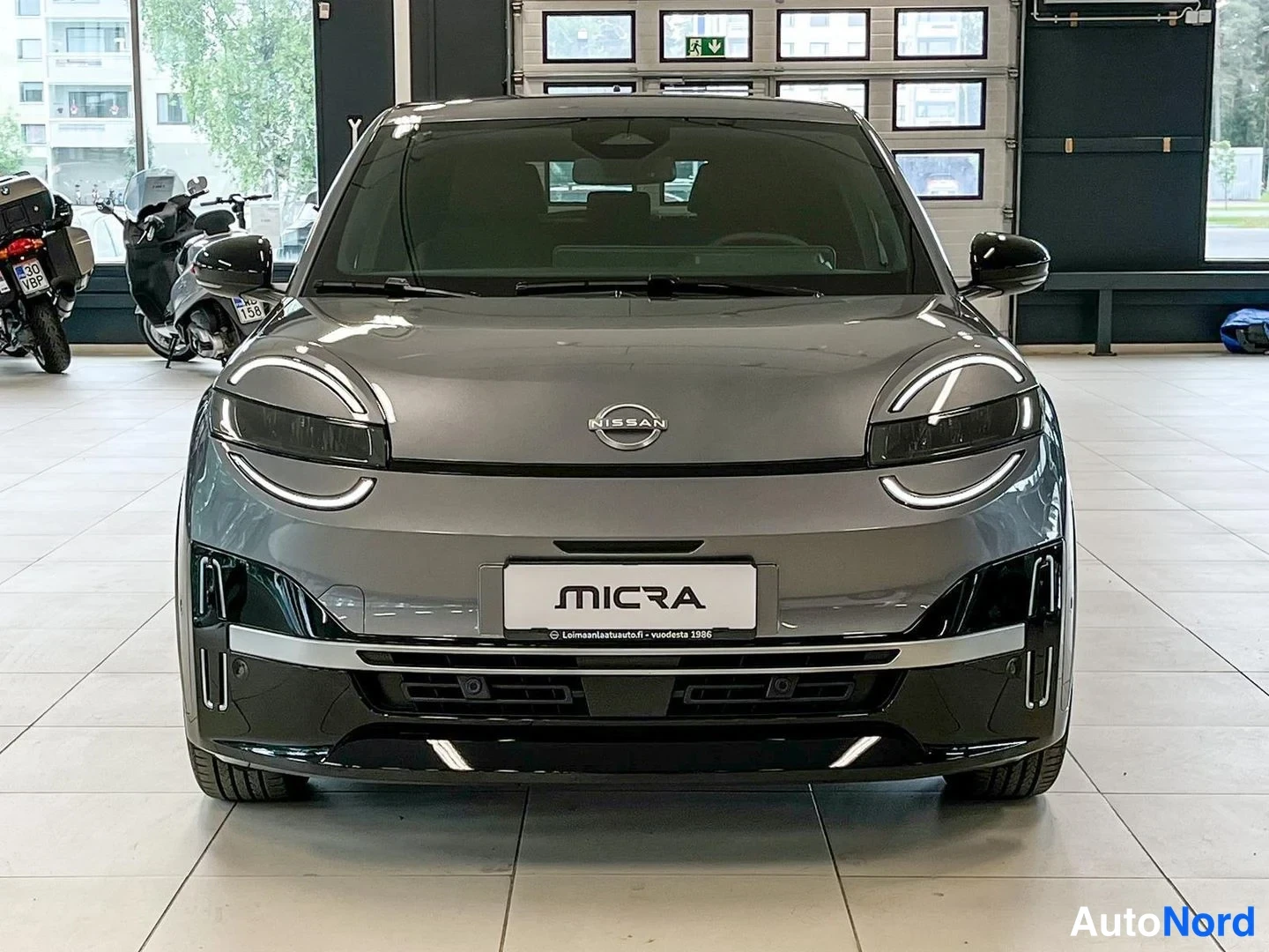 Edestä: Nissan Micra -henkilöauto harmaana suoraan edestä, kyltillä MICRA.