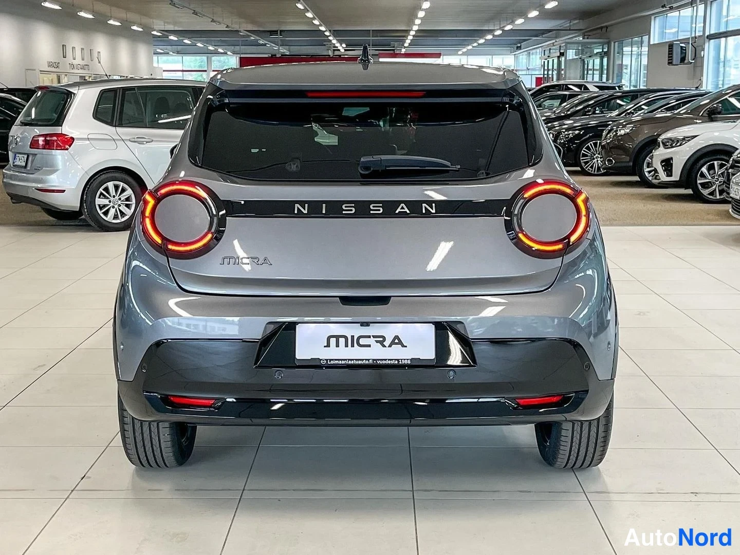 Takaa: Nissan Micran takaosa suoraan takaa; pyöreät takavalot, NISSAN-tekni ja MICRA-kyltti luukussa, harmaa kori.