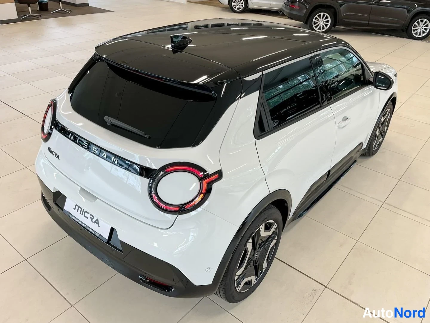 Takaviisto: Valkoisen mustakattoisen Nissan Micran takakulma yläviistosta, takavaloja ja NISSAN-teksti näkyvissä.