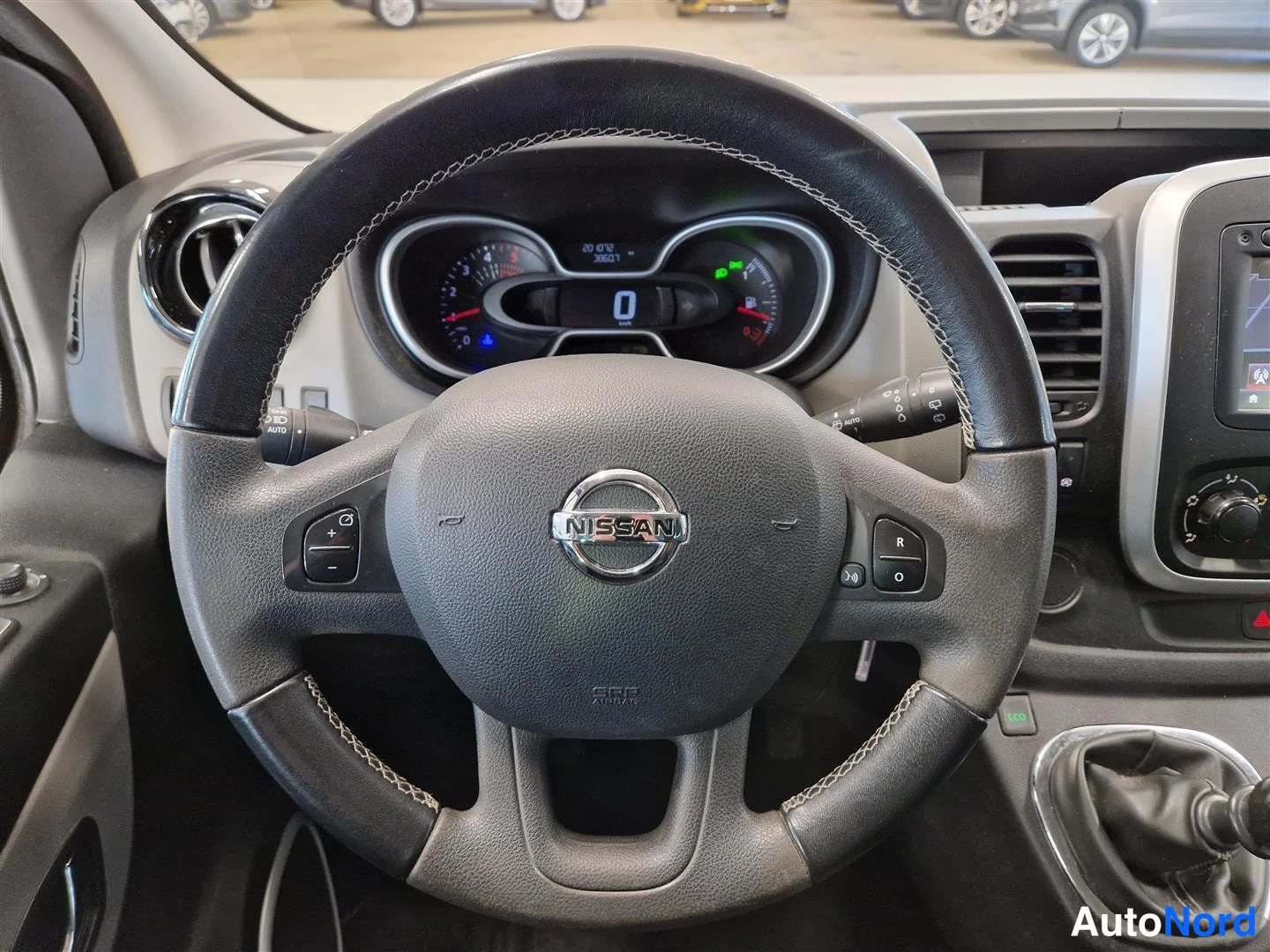 Sivulta: Ohjaamoon näyttävä kuva: Nissan-merkillä varustettu ohjauspyörä, mittaristö näytöllä, jossa lukee 0 km, manuaalivaihteen keila ja kojelaudan säätimiä.