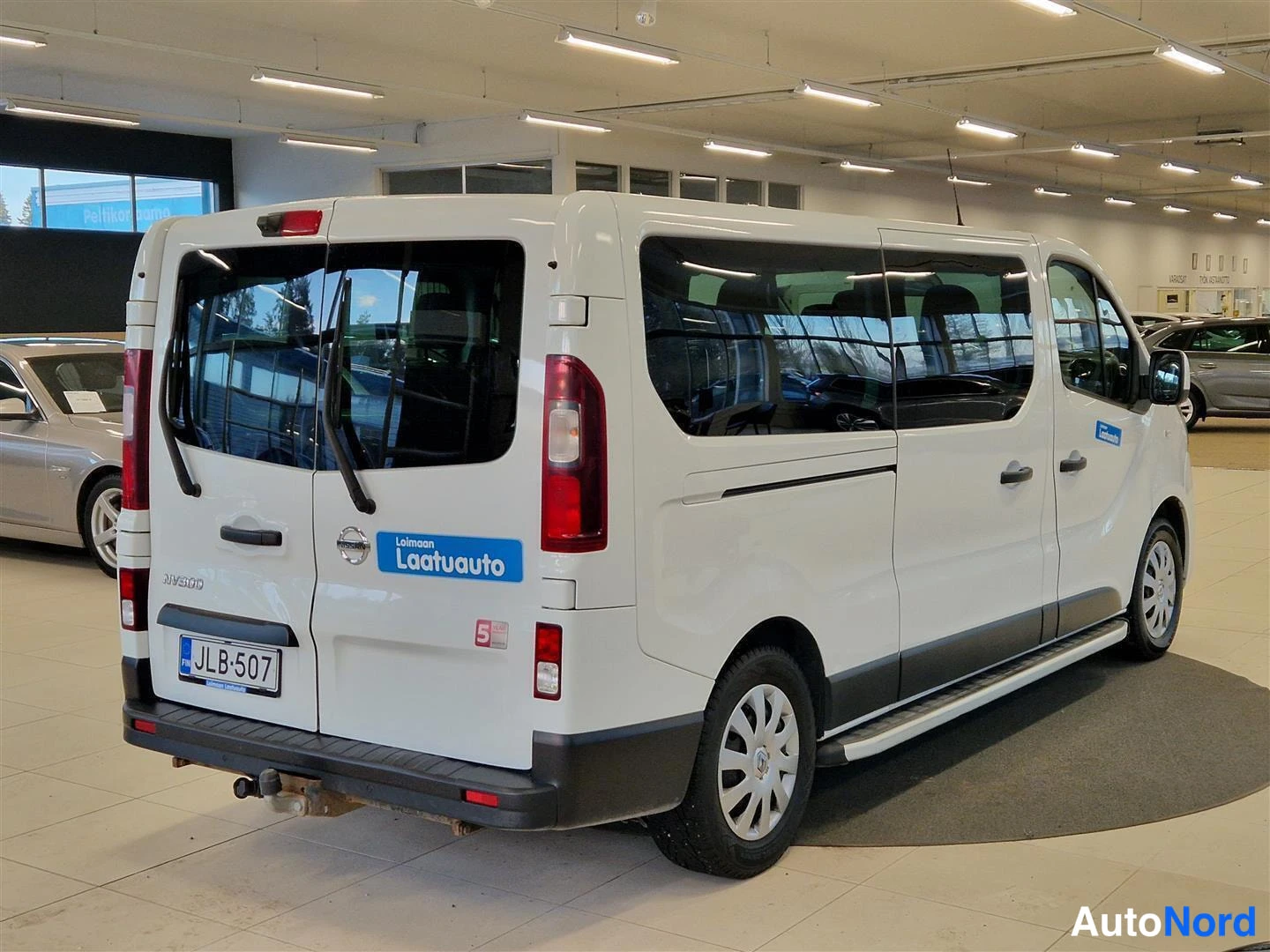 Takaviisto: Valkoisen Nissan NV300 -pakettiauton takaosa ja vasen sivu; takavalot, takaluukut, rekisterikilpi ja kytkentaarat näkyvät.