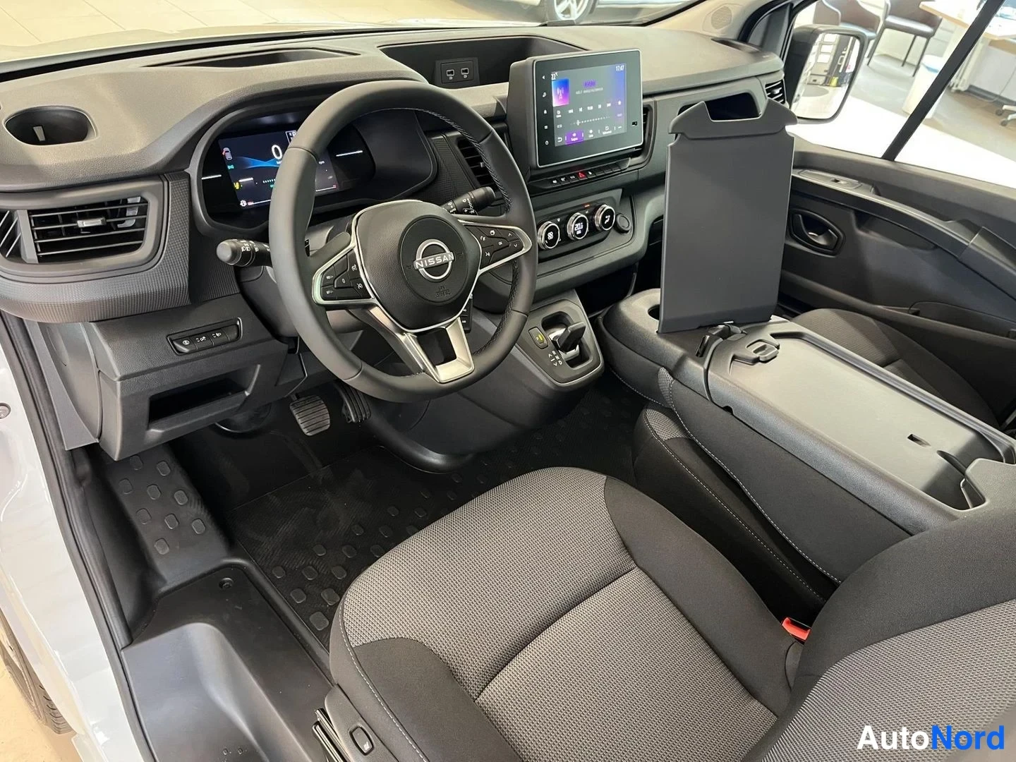Sivulta: Ohjaamo kuljettajan puolelta: Nissan-merkkinen ohjauspyörä, digitaalinen mittaristo, kosketusnäyttö ja automaattivaihteen valitsin.