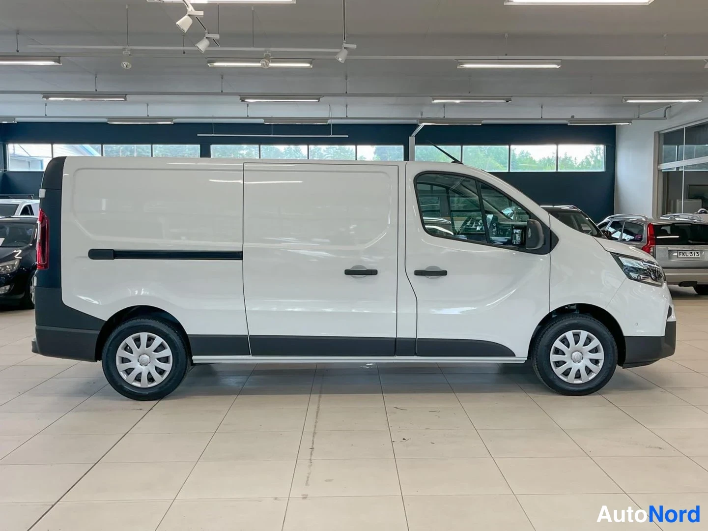 Takaviisto: Valkoinen Nissan Primastar -pakettiauto takakulmalta vasemmalta, liikehallissa.