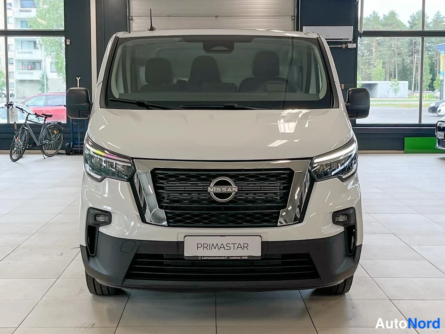 Edestä: Nissan Primastar -pakettiauto suoraan edestä, valkoinen, liikehallissa.
