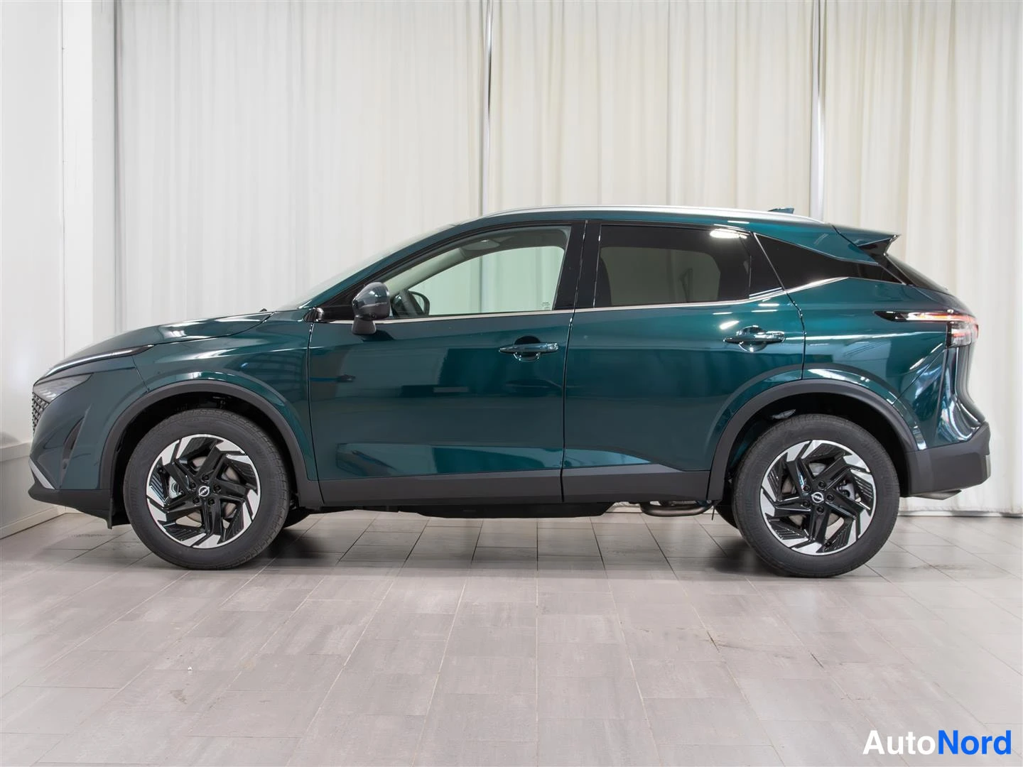 Etuviisto, nokka vasemmalle: Tummanvihreä Nissan Qashqai -tyyppinen automobiili kuvattu kolmasosakulmasta etuosan osoittaessa vasemmalle, kuvattu studiomainen valkoinen tausta.