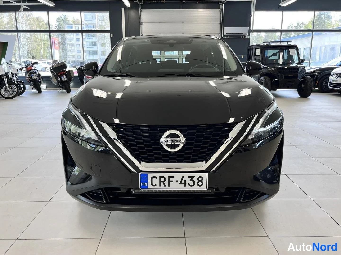 Edestä: Edessä suoraan kuvattu musta Nissan, verkkokori ja Nissan-merkki keskellä, rekisterikilpi.