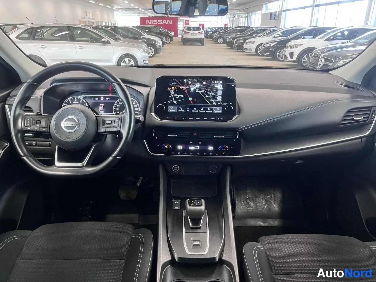 Asiakirja: Ohjaamo mustasta sisustasta: Nissan-ohjauspyörä, digitaalinen mittaristo, kartta näytöllä oleva infotainment-näyttö, automaattivaihteen valitsin ja kankaiset et