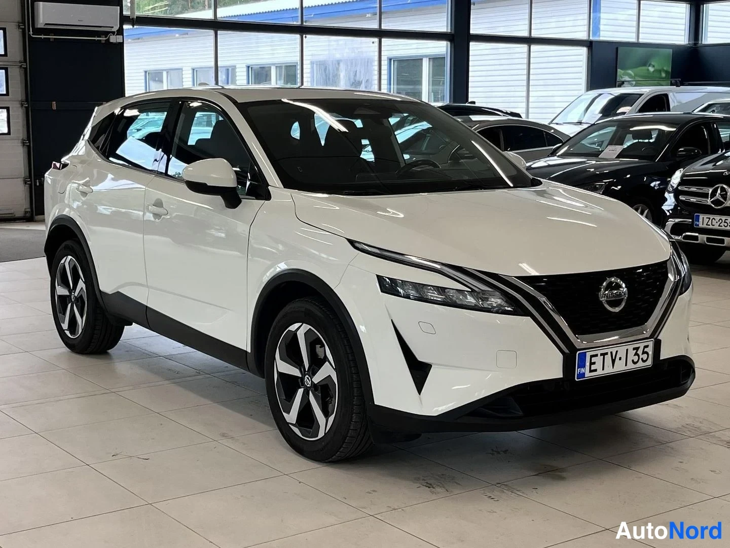 Etuviisto, nokka oikealle: Valkoinen Nissan Qashqai kulmassa edestä oikealta näkyvästi autosalissa, rekisterikilpi.