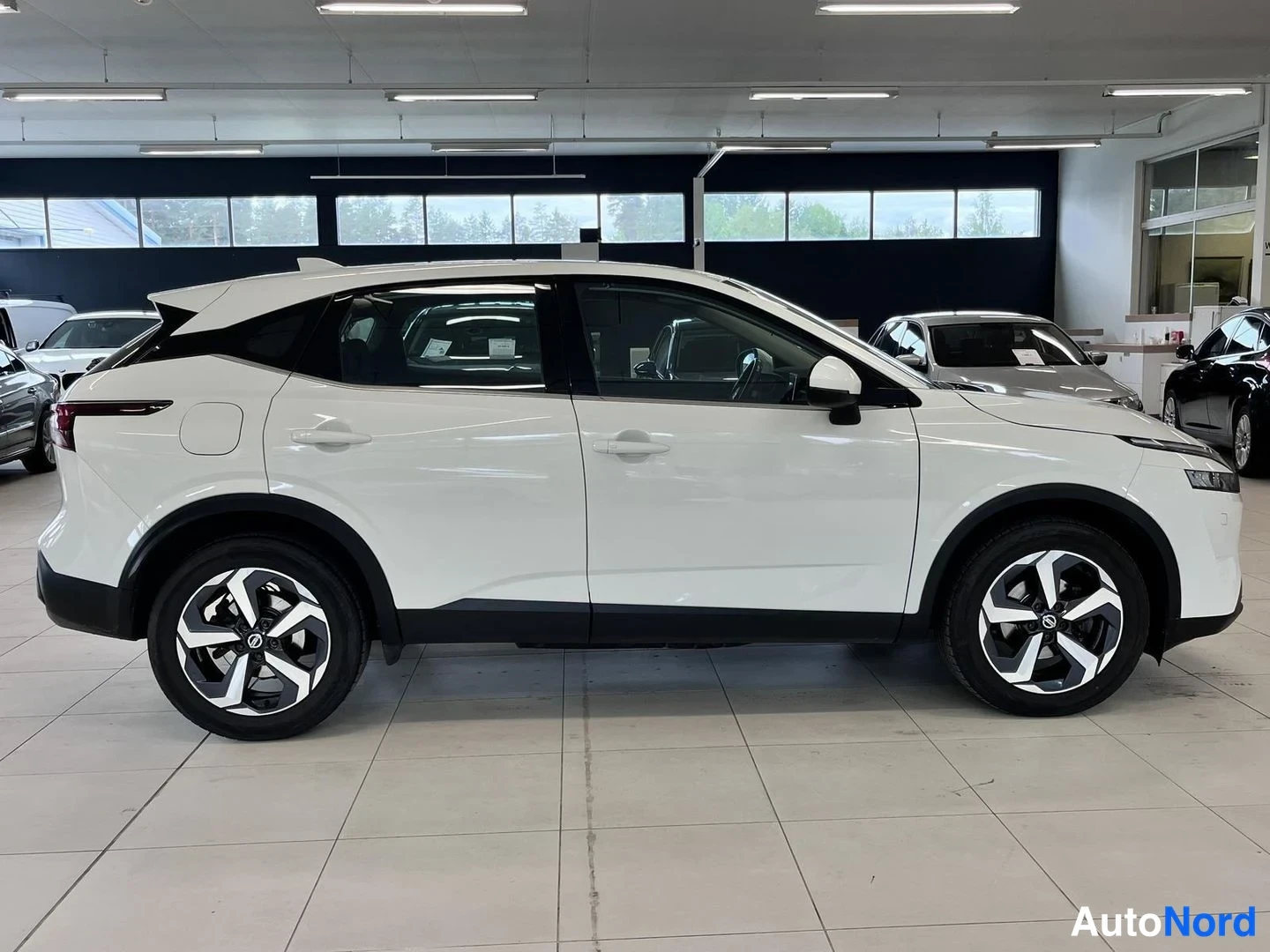 Sivulta: Valkoinen Nissan Qashqai sivulta näkyvästi autosalissa, vasen kylki kuvassa.