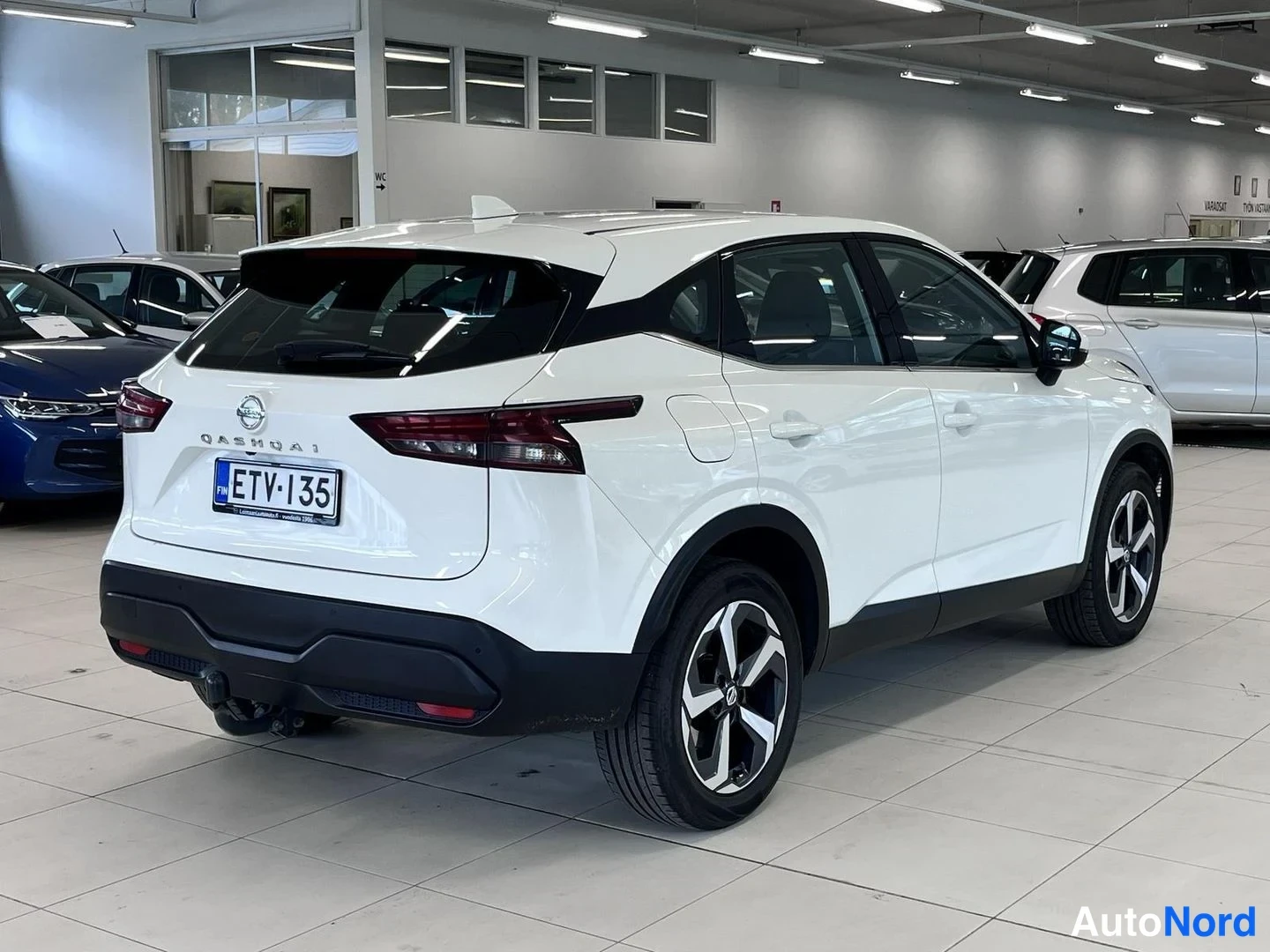 Takaviisto: Valkoisen Nissan Qashqain takakulman kuvakulma myymälähallissa; rekisterikilpi, takavalo ja vetokoukku näkyvät.