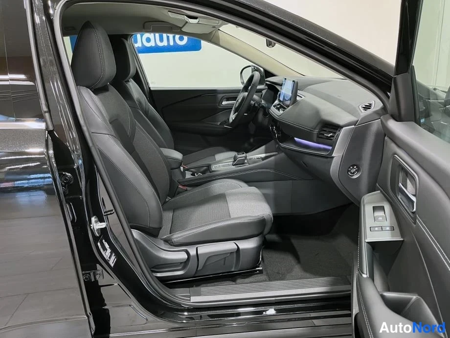 Muu: Nissan Qashqain sisätilat näkyvät avoimesta kuljettajan ovesta: mustat kangasistuimet, ohjauspyörä, kojetaulun näyttö ja vaihdin.