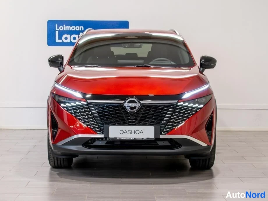 Edestä: Punaisen Nissan Qashqain etupää kuvattuna suoraan edestä; näkyvissä etusäleikkö, Nissan-merkki, ajovalot ja QASHQAI-kyltti.