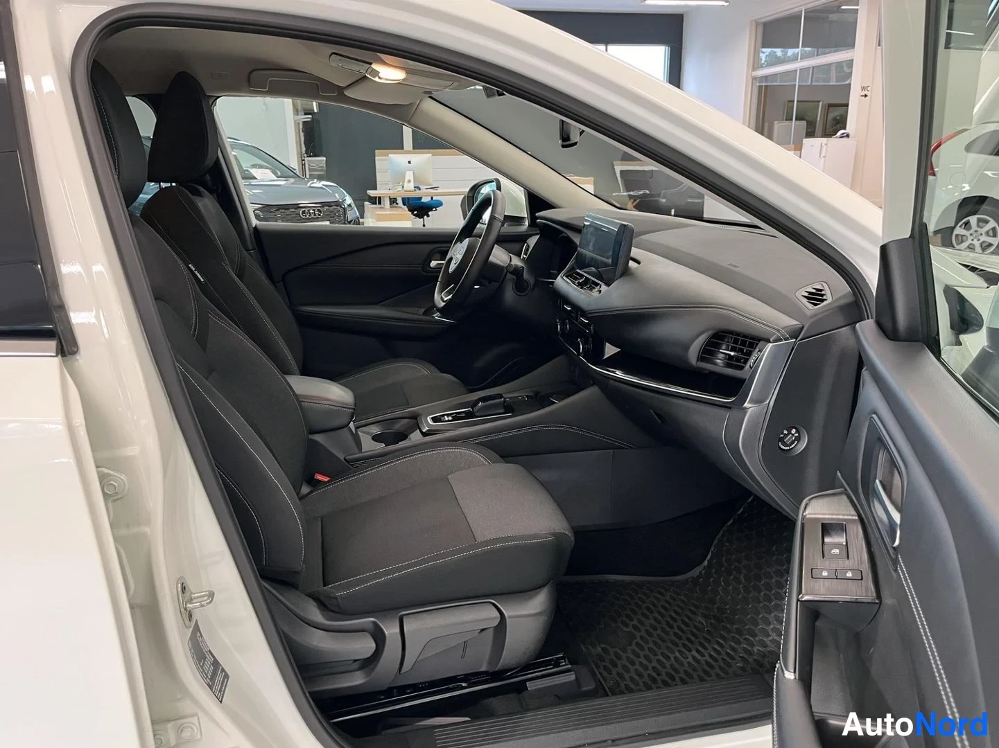 Muu: Nissan Qashqain etumatkustustila avoimesta oikeasta etiovesta: tumma kankainen etuistuin, ohjauspyörä ja keskinäytöllinen kojelauta.