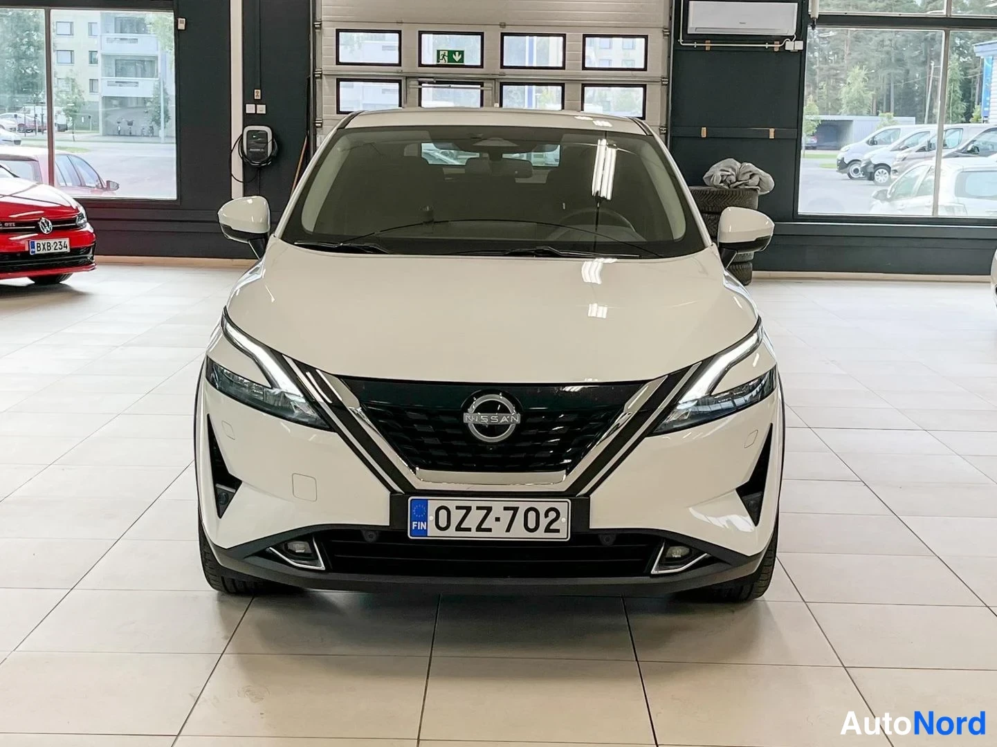 Edestä: Nissan Qashqai -näkymä edestäpäin myyntihallissa, valkoinen koripaneli, etumoottoritilan säleikkö ja logot sekä rekisterikilpi näkyvät.