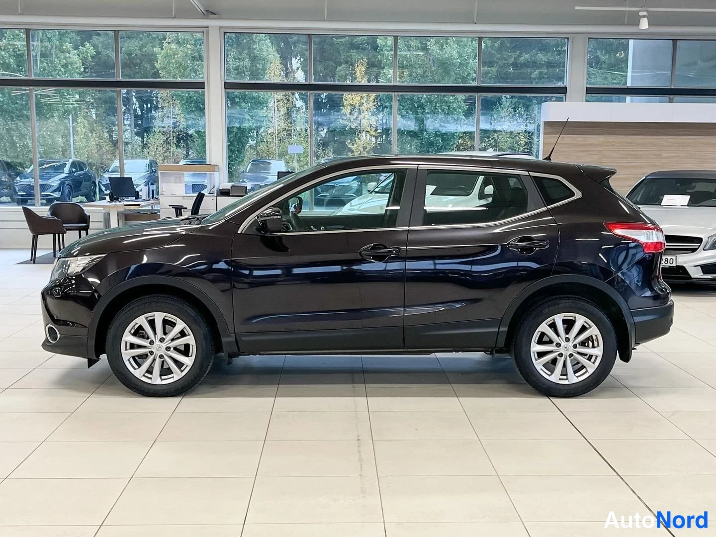Sivulta: Tummanvioletti Nissan Qashqai -henkilöauto sivuprofiilista autonäyttelytilassa, keula vasemmalla.