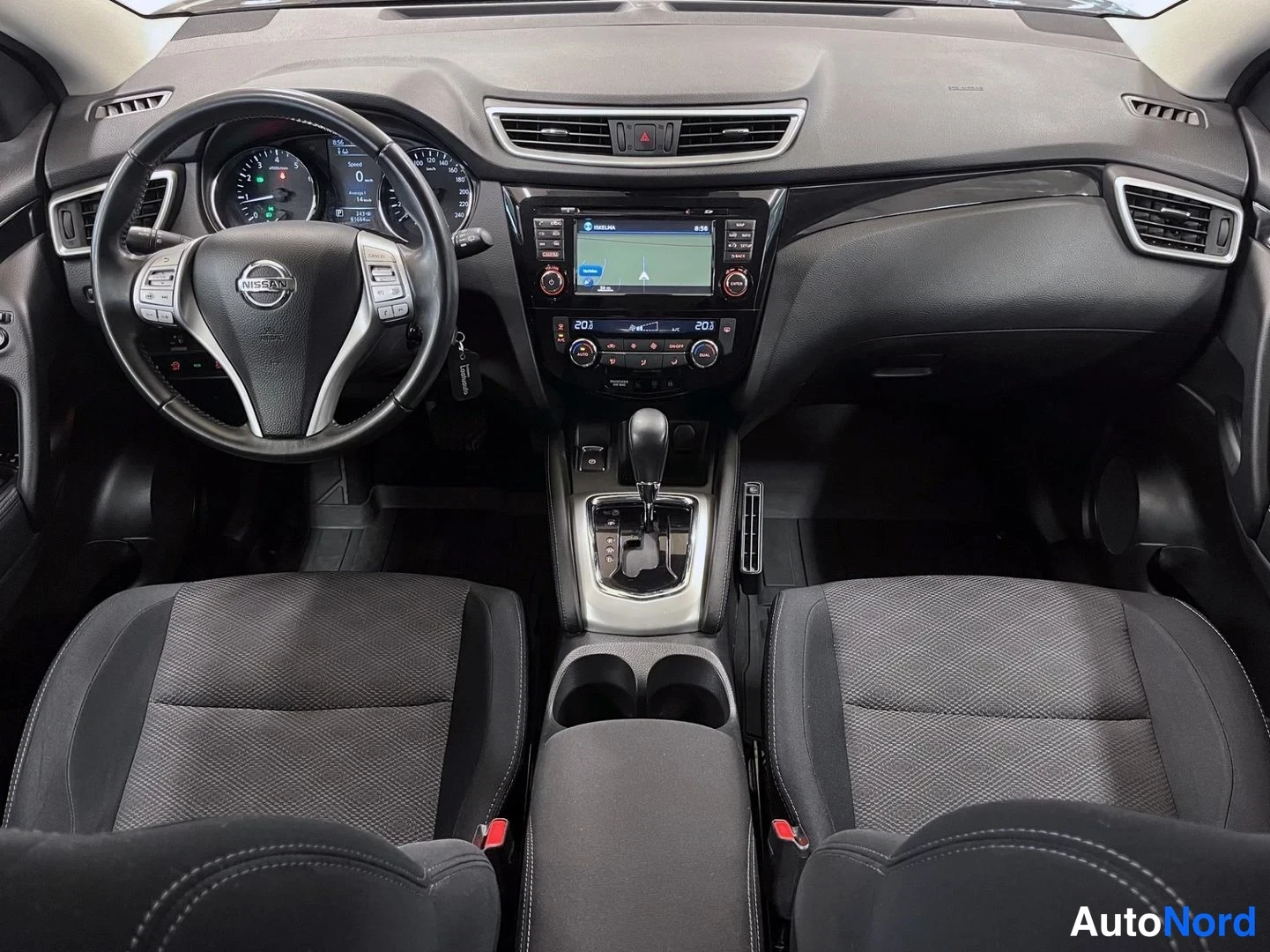 Muu: Ohjaamo kuvattuna takaa: Nissan-ohjauspyörä, analogiset mittarit, keskikonsolin näyttö ja automaattivaihteen valitsin, mustat kangasistuimet eturivissä.