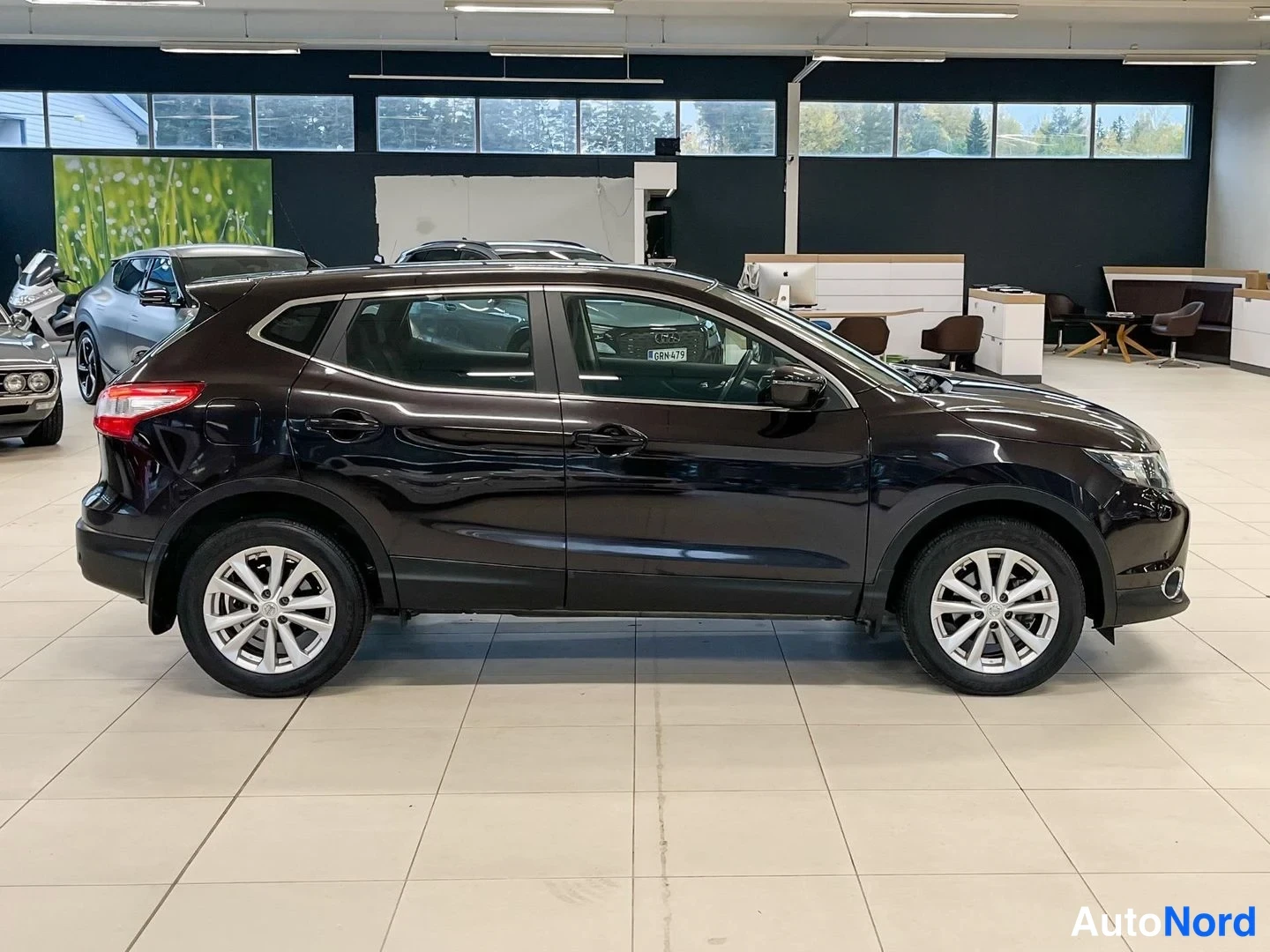 Takaviisto: Tummanvioletti Nissan Qashqai -henkilöauto takakulmanäkymänä autonäyttelytilassa, perä vasemmalla.