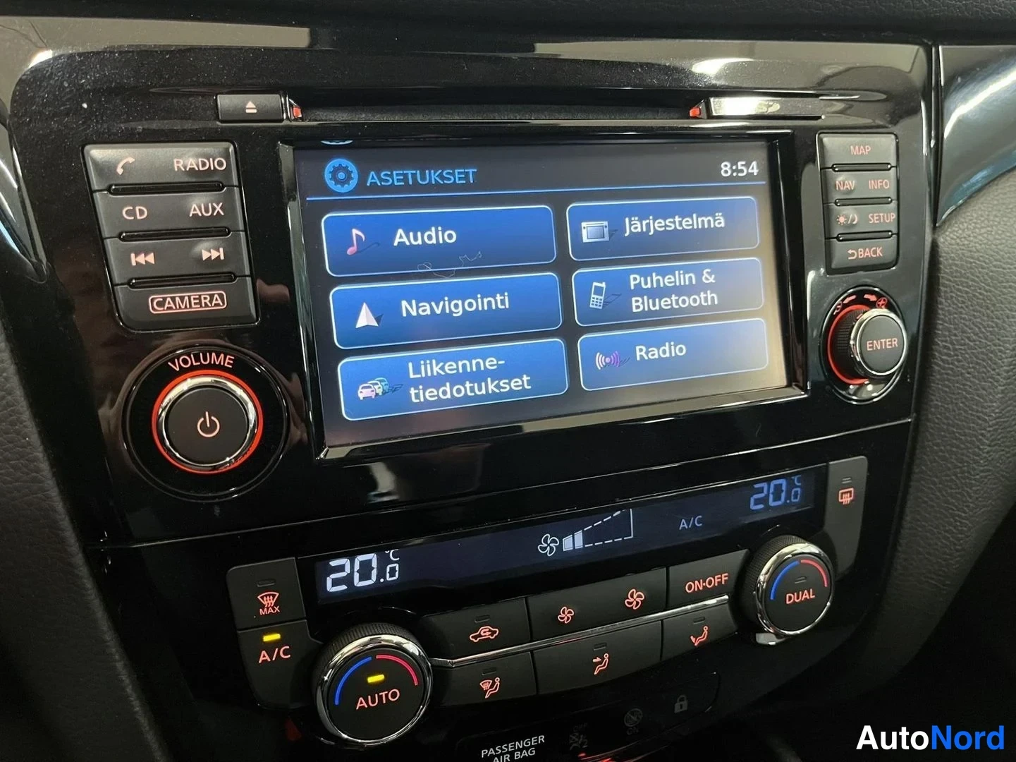Yksityiskohta: Asetukset-valikko näytöllä: vaihtoehdot Audio, Järjestelmä, Navigointi, Puhelin & Bluetooth, Liikennetiedotukset ja Radio; radio- ja ilmastointipainikkeet ja 20