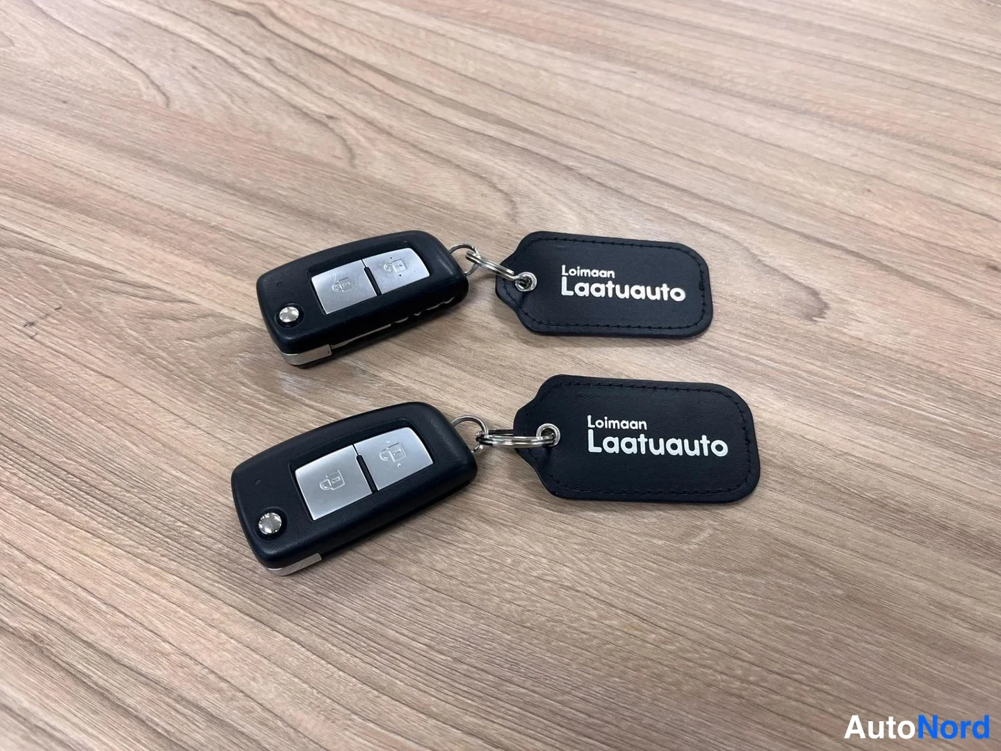 Muu: Kaksi auton kauko-ohjainavainta tunnisteilla Loimaan Laatuauto puupöydällä.