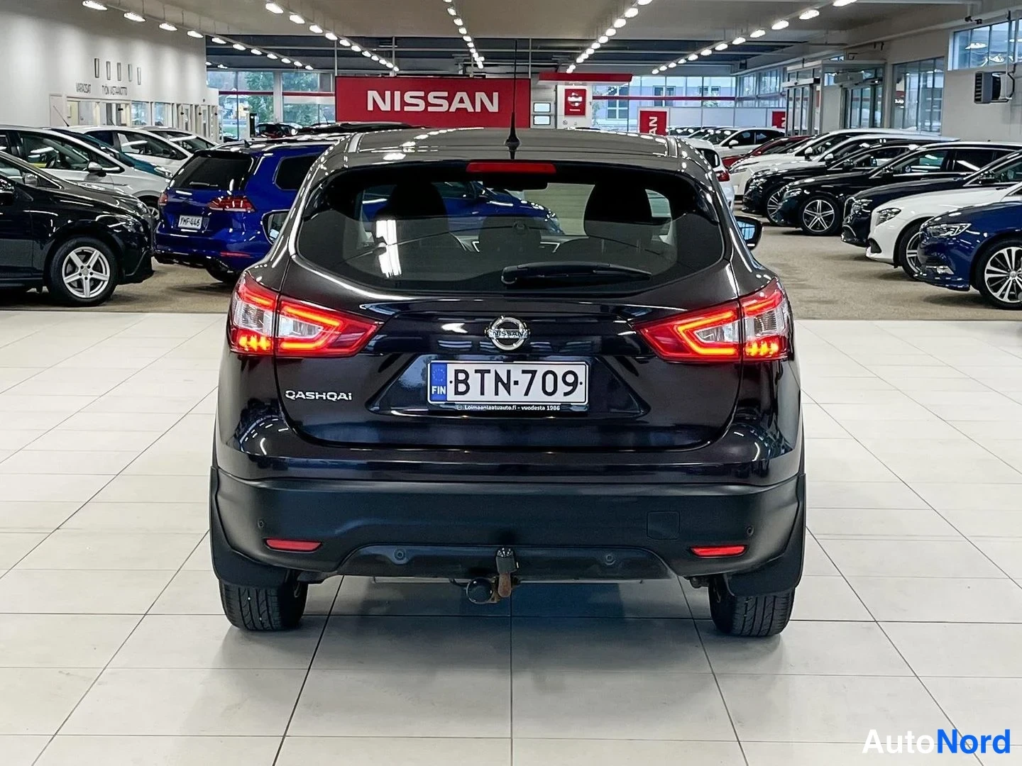 Takaa: Auton takanäkymä myyntihallissa: tumma Nissan Qashqai, rekisterikilpi, takavalot ja lukittu vetokoukku näkyvissä.