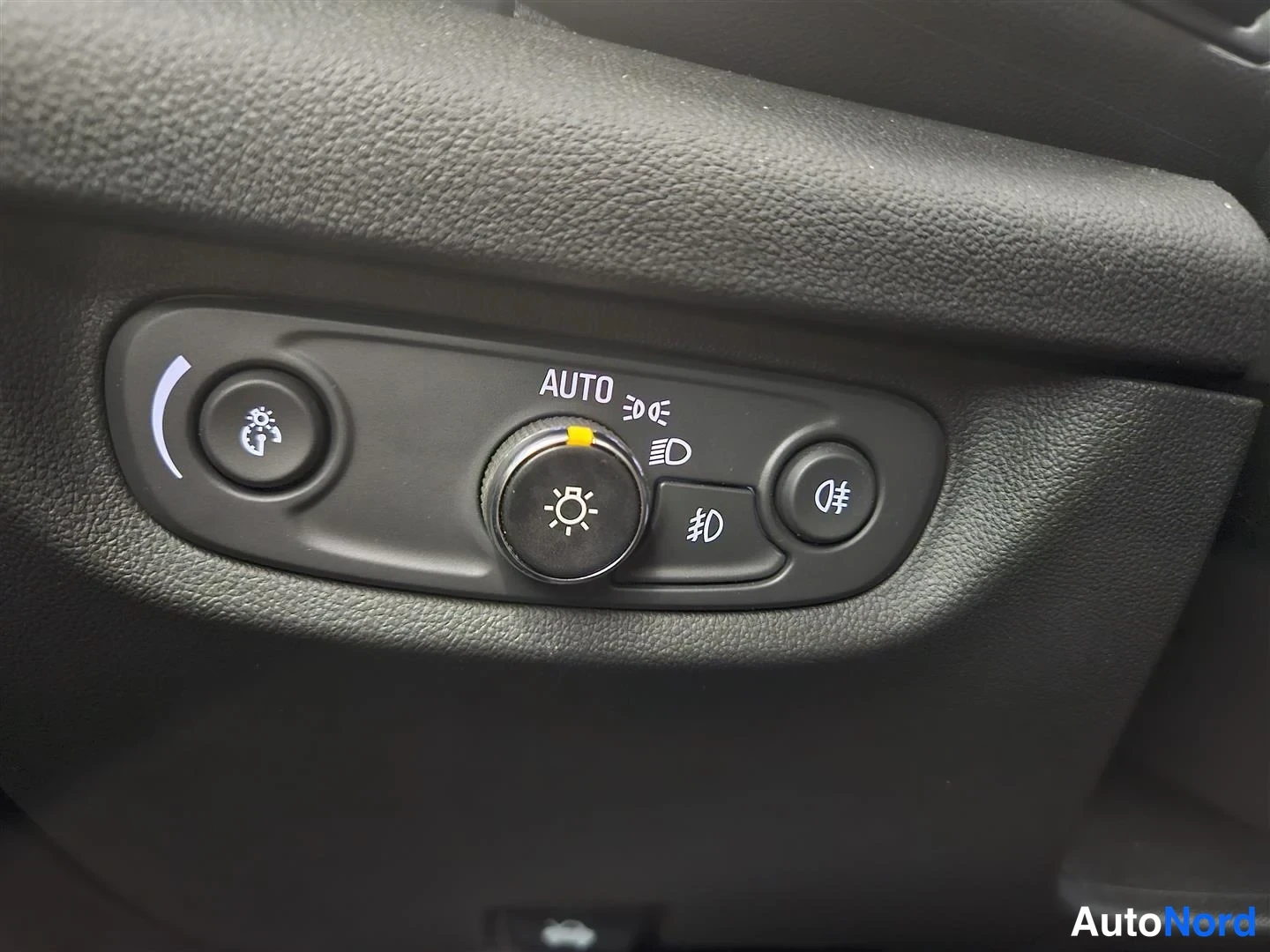 Yksityiskohta: Auton valokytkinpaneeli, jossa AUTO-merkitty säädin, sumuvalot-nappi ja instrumentti-nappi.