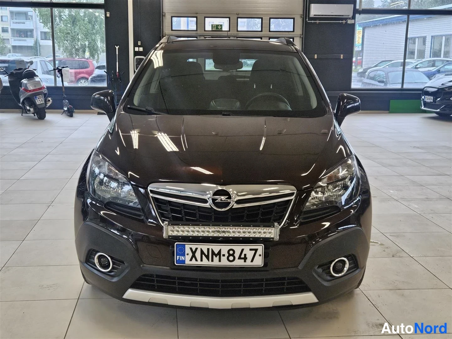 Edestä: Opel Mokka suoraan edestäpäin, Opel-merkki jäähdytinsäleikössä, LED-palkki ja rekisteri, autosalon sisätiloissa.