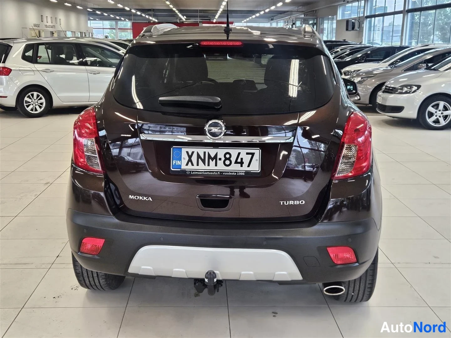 Takaa: Opel Mokka:n takaosa näkyy suoraan takaa; tummanruskea kori, takavalot ja rekisterikilpi näkyvät sisätiloissa.